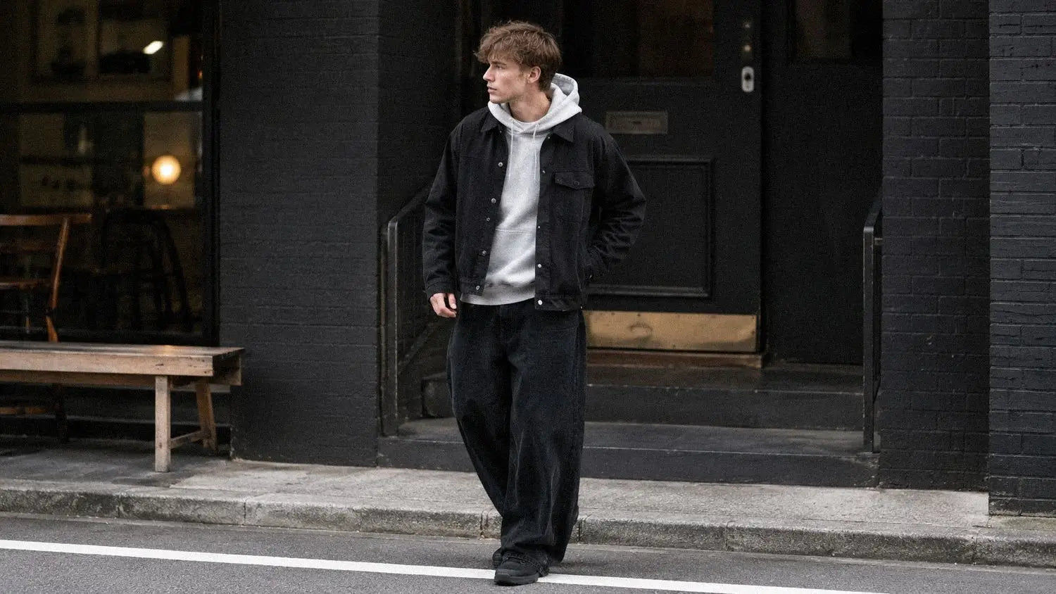 Black trucker jacket over a grey hoodie showing accent contrast within a dark streetwear outfit