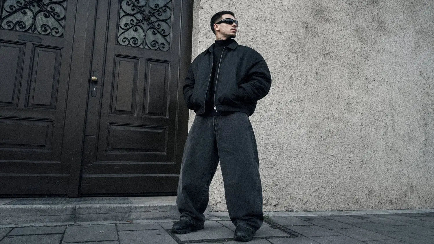 Cropped black bomber jacket paired with extremely wide jeans in a balanced dark streetwear fit