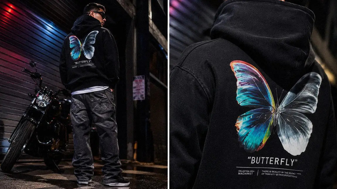 Black streetwear hoodie with a colorful butterfly graphic worn beside a motorcycle at night