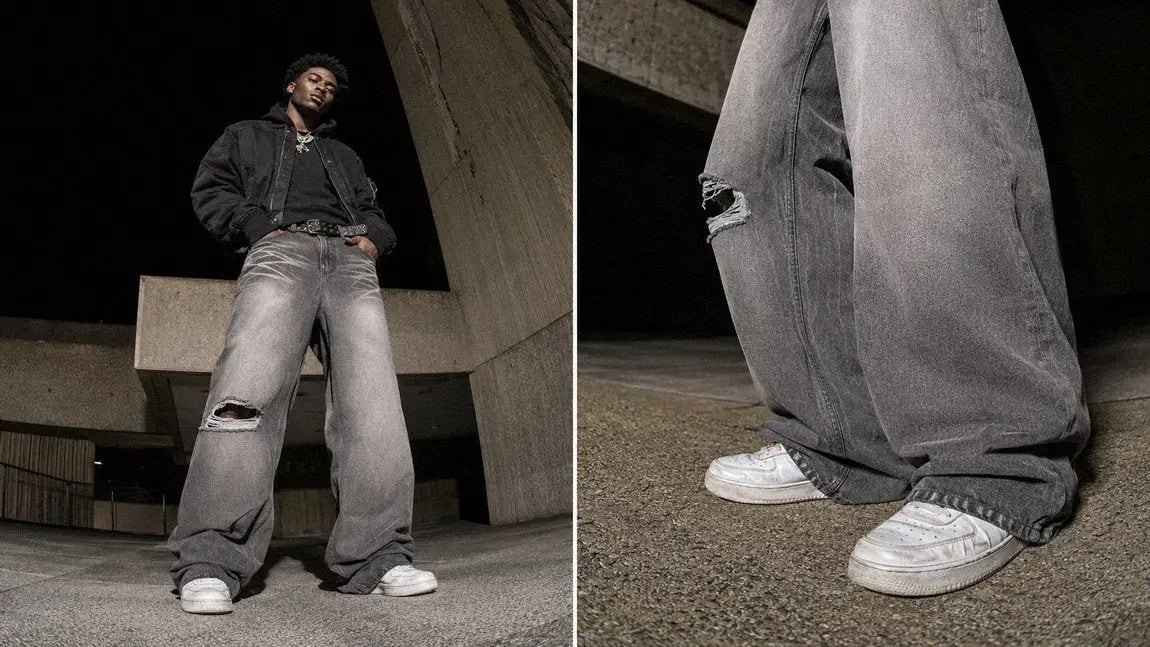 Wide grey-wash streetwear jeans with a ripped knee shown against brutalist architecture