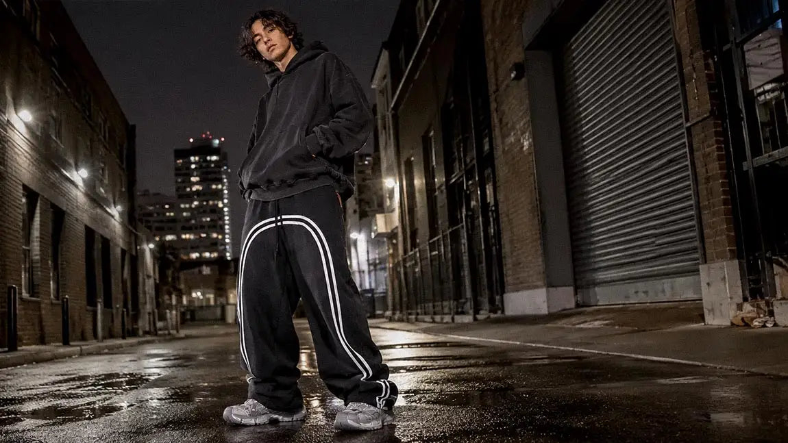 Black streetwear sweatpants with a double side stripe worn with an oversized hoodie at night
