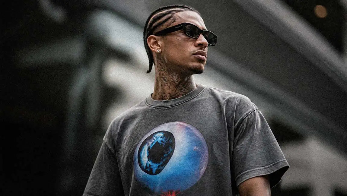 Braided hair and black sunglasses complete this look featuring a grey Streetwear t-shirt with an eye graphic.