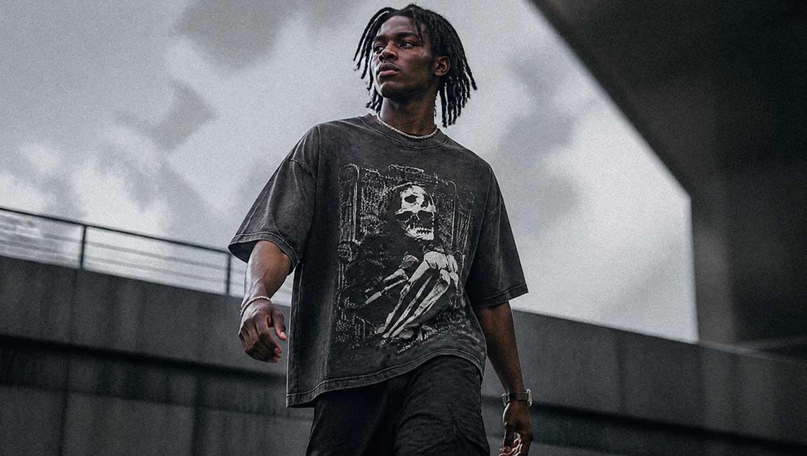 The model walks through a brutalist location wearing a dark Streetwear t-shirt with a skeleton print.